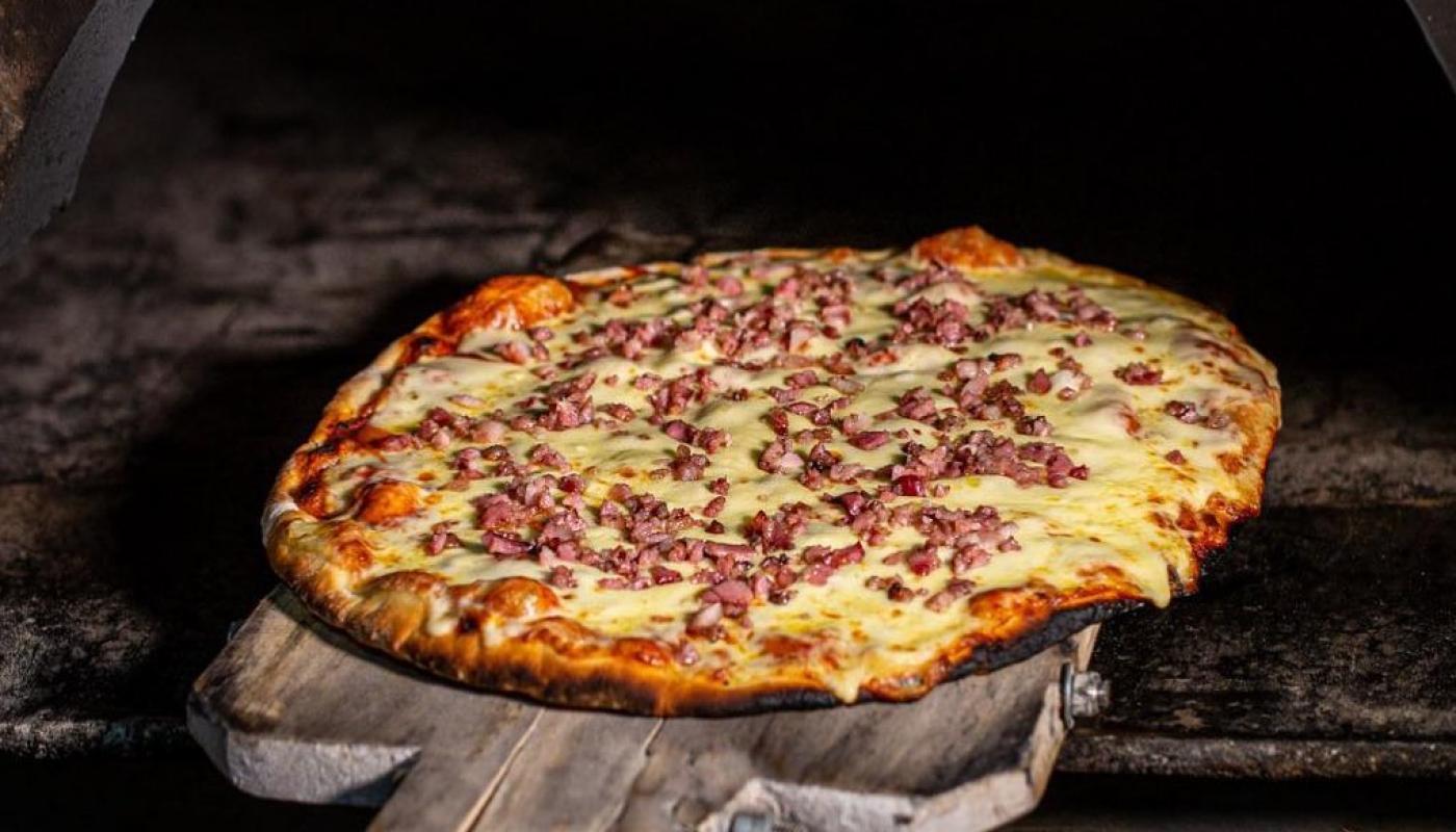 primer plano de horno oval con tabla con pizza con gustos pronta para sacar del horno y comer
