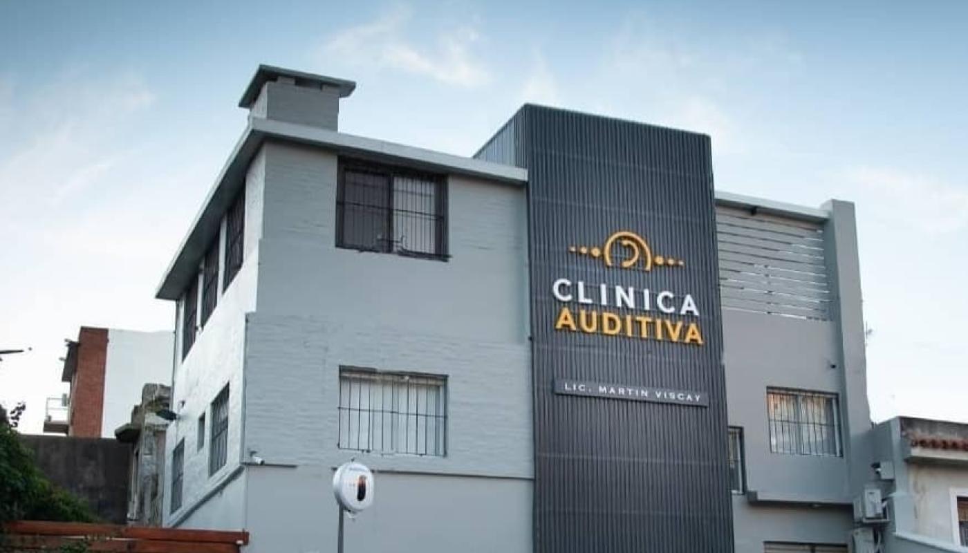 Sede de la empresa. Casa moderna en color gris de dos pisos con reja al frente. Cartel con nombre de la empresa en blanco y amarillo a lo largo de la fachada. 