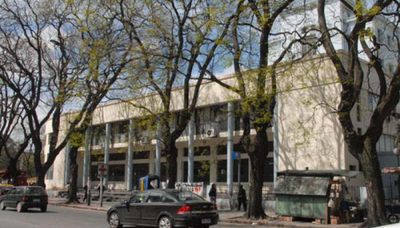 Fachada principal a la calle. Cuadra muy arbolada. Edificio moderno en color crema. Estructura vidriada con columnas. Ingreso con escalinata. 