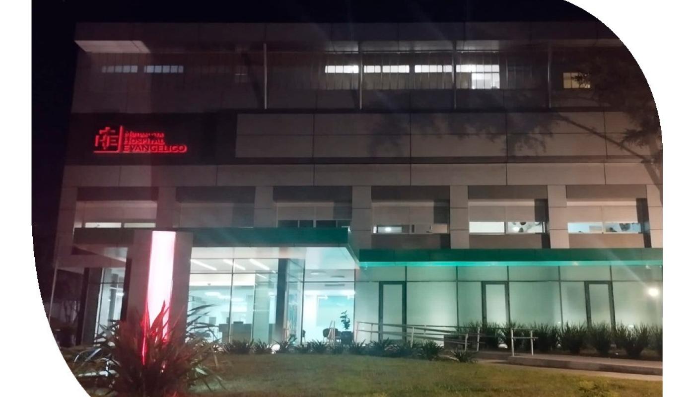 Foto nocturna de la mutualista y su sede principal. Edificio moderno vidriado con jardín al frente. 