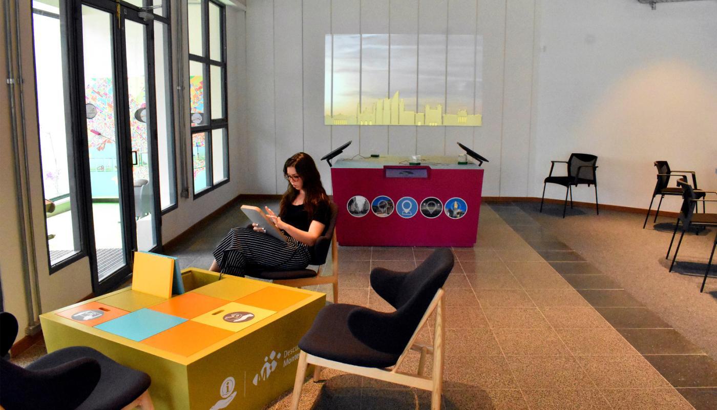 visitante sentado en la oficina de información Turística vidriada utilizando las tablets brindadas por el Servicio. Al fondo se encuentra una mesa interactiva
