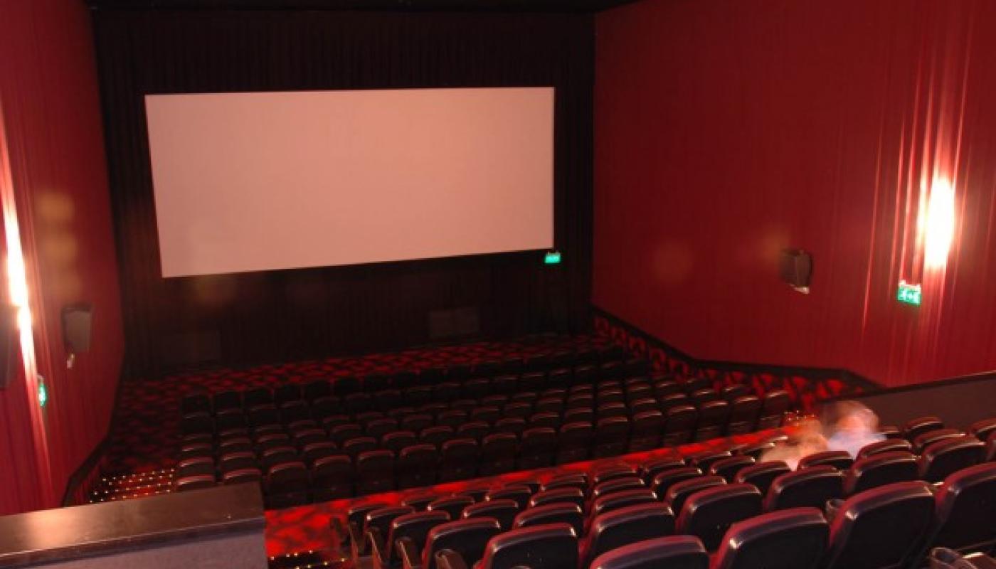 Foto desde atrás con las butacas rojas en dos niveles y pantalla para proyectar al frente. 