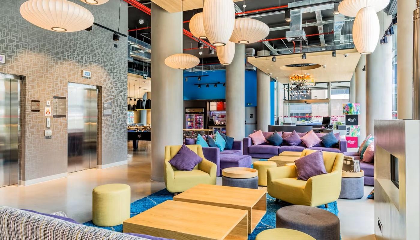 Lobby del hotel. Hay sillones de diversos tamaños y colores. Al fondo hay una mesa de pool, una heladera con bebidas y mesas con sillas.