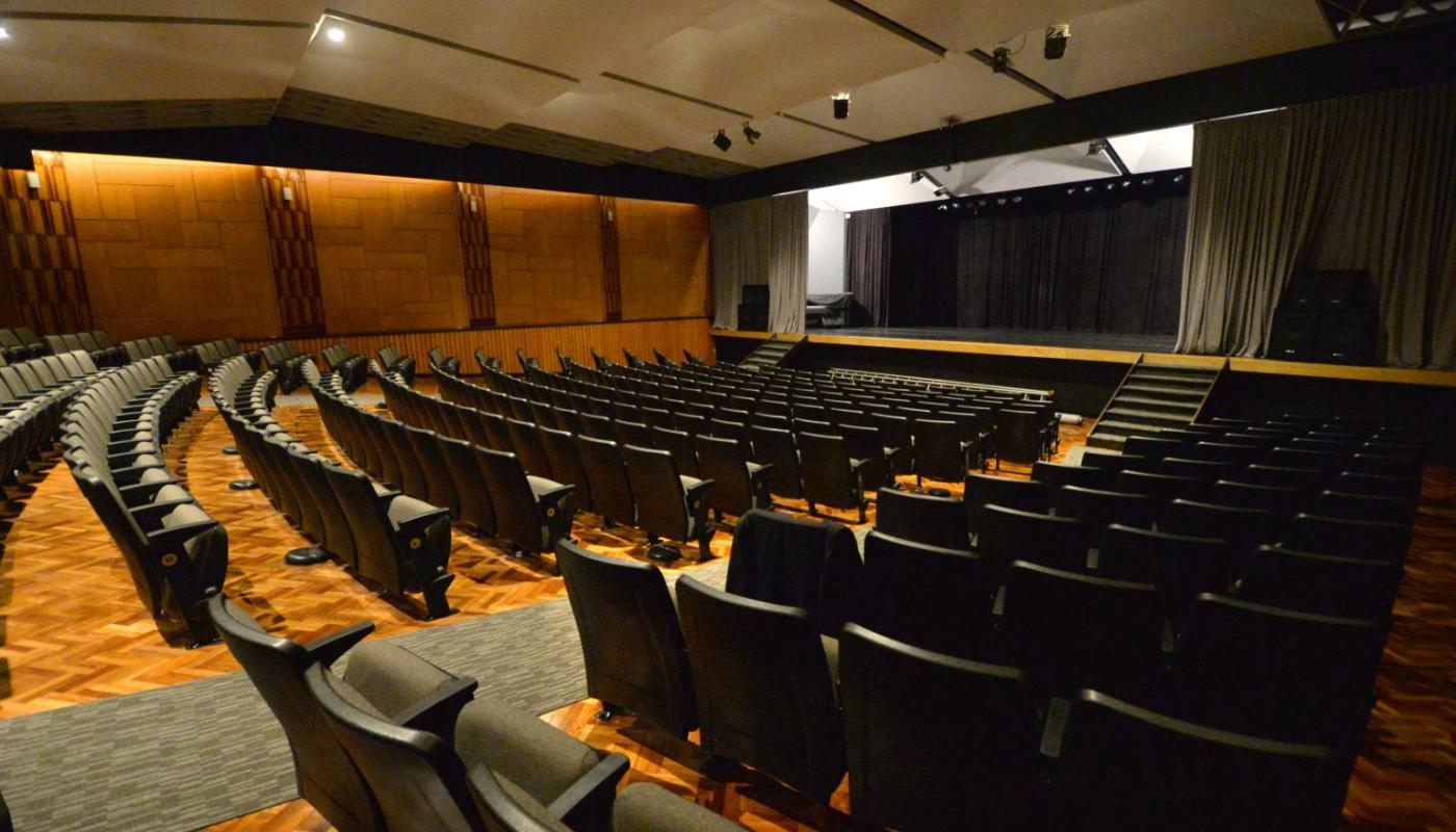 sala del auditorio con butacas color negro sobre piso de madera claro enfrentadas a escenario grande con telones y en altura
