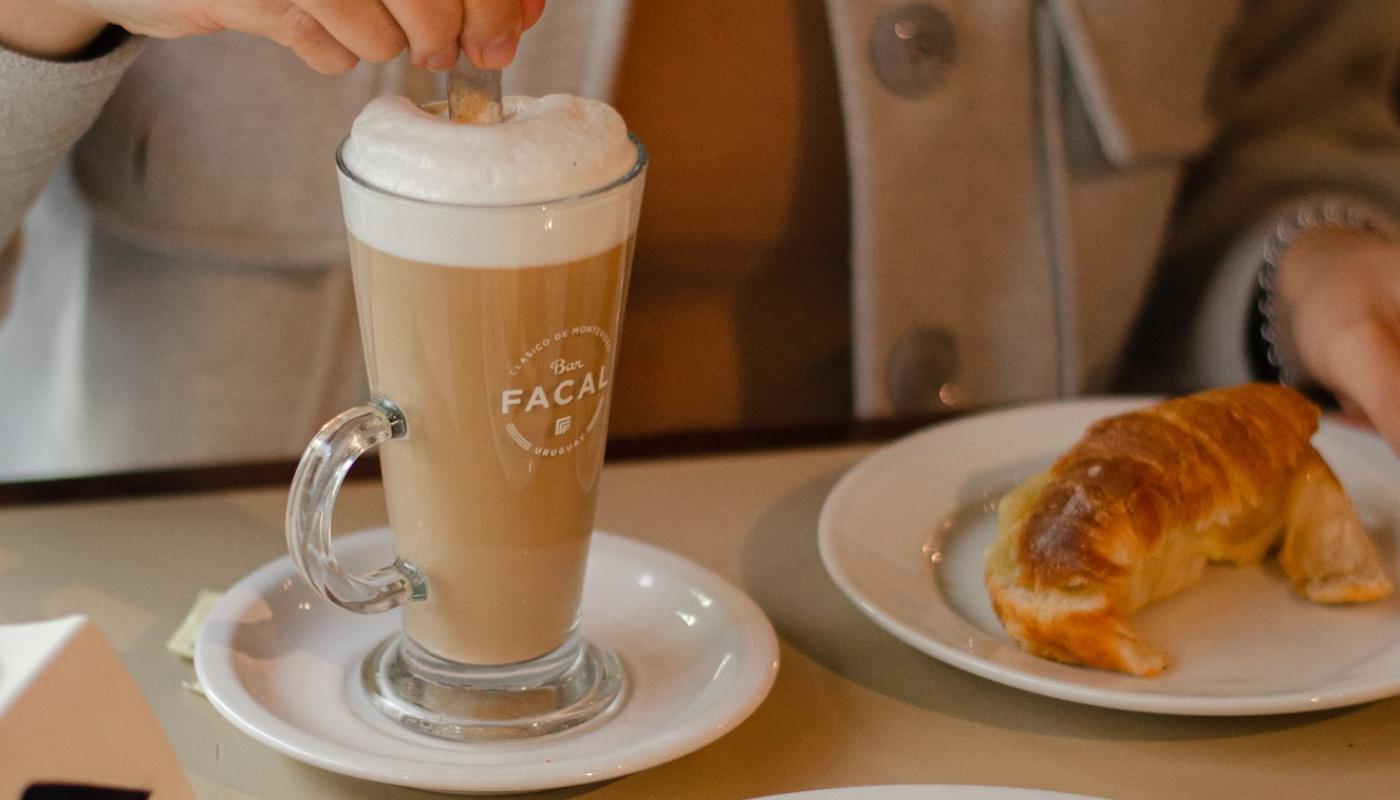 merienda bar facal: persona tomando un capuchino con medialunas y sandwiches