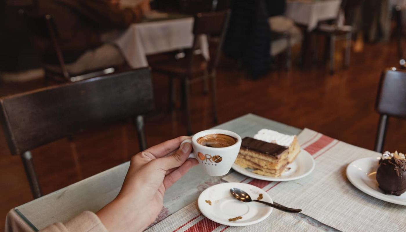 primer plano de mujer merendando una torta de cafe al fondo el local de varias mesas decorado con maderas antiguas