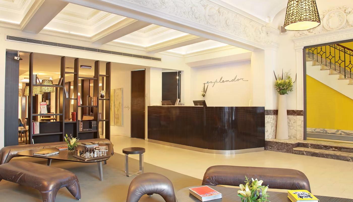  Lobby del hotel. Hay varias banquetas de cuero de distinto tamaño, una mesa ratona de vidrio triangular y, al fondo, el mostrador de atención al público.   