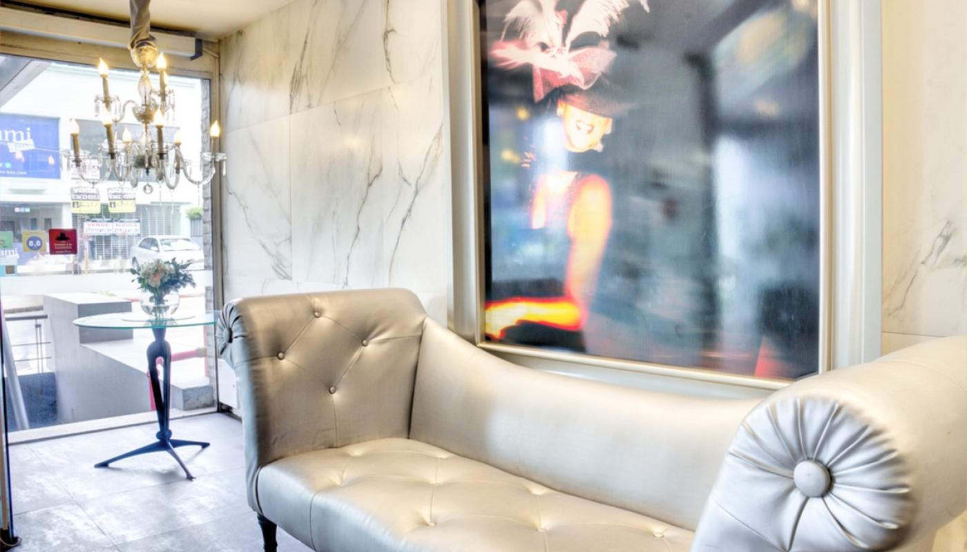 Hall de ingreso del hotel Regency Golf. Piso y pared de mármol blanco. Diván plateado, araña de techo de cristal, mesita de vidrio redonda con florero pequeño, gran cuadro con imagen de bailarina de cabaret.