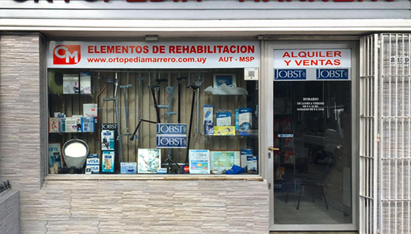 Foto de fachada de la ortepedía con el nombre de la empresa en rojo. Ventana y puerta con reja. Pequeño local a la calle. 