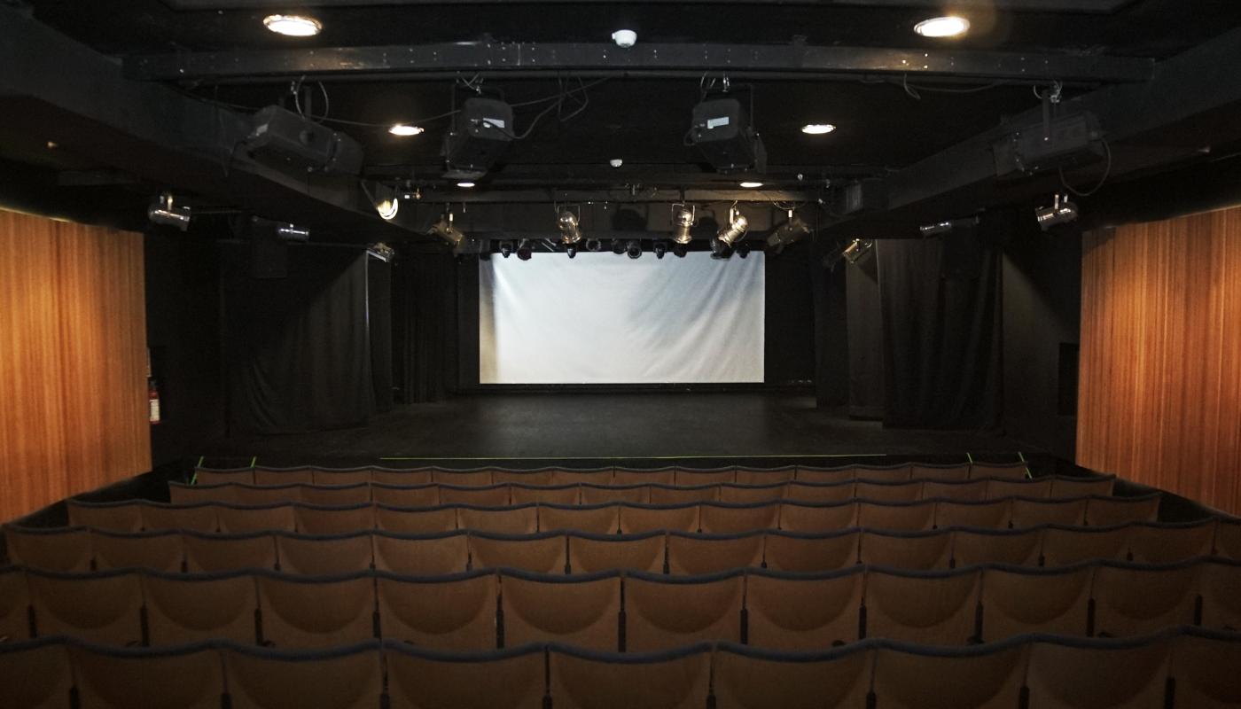 Sala principal con butacas beiges. En los costados paneles de madera para la acústica. Al frente escenario y pantalla para proyectar.