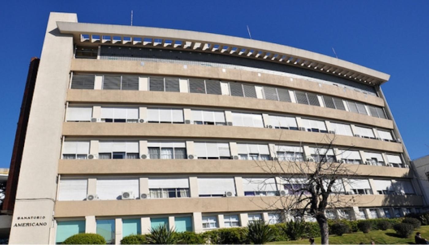 Edificio moderno con varios pisos de colores claros. Jardín al frente. 