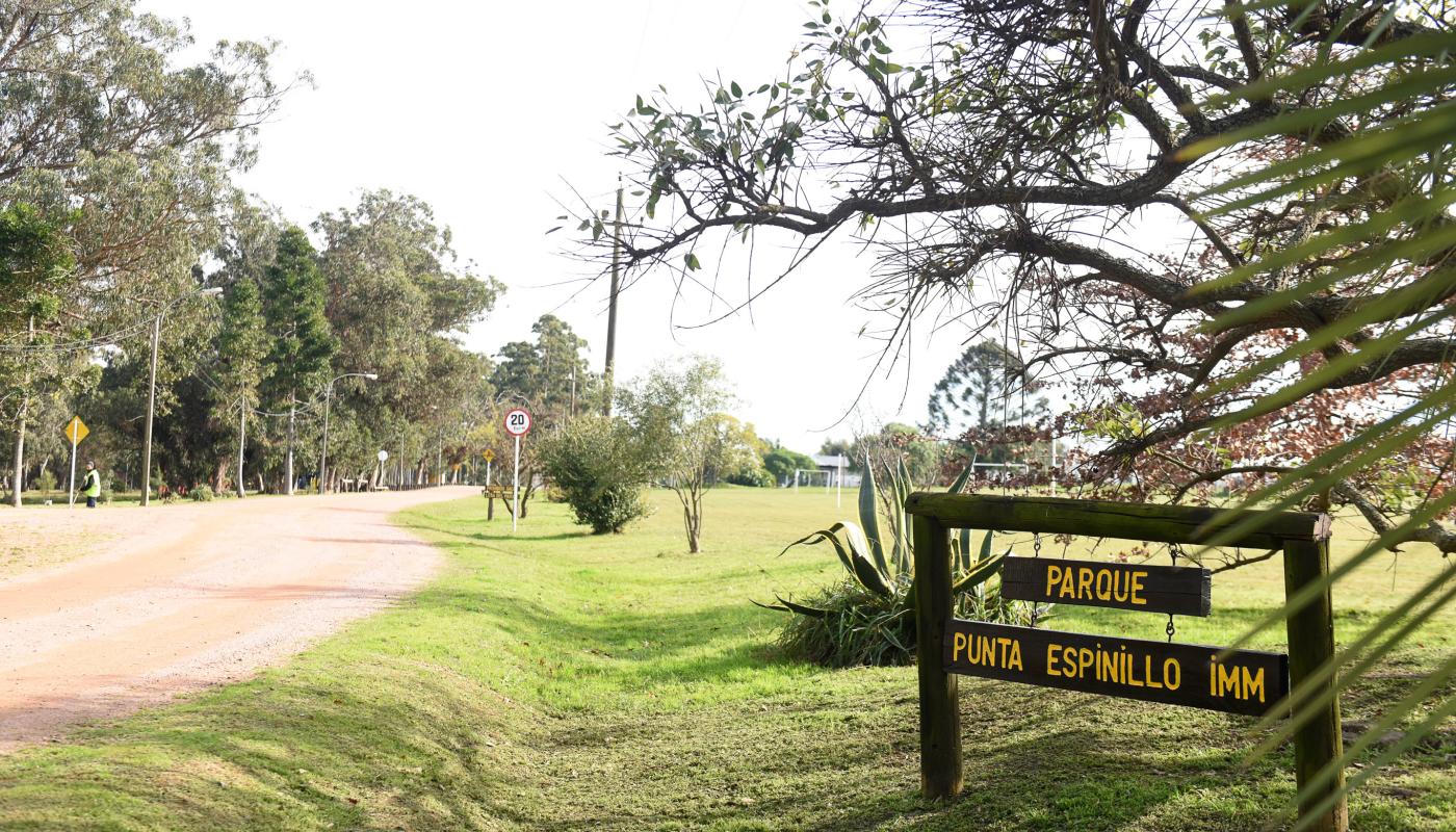 foto de entrada al parque , al frente cartel de madera sobre ceped con nombre del lugar. Espacio grande y verde arboaldo