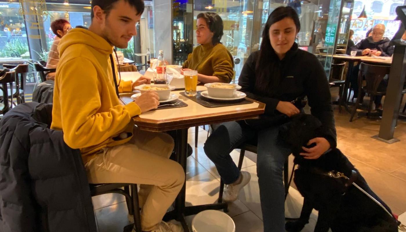 Foto del Bar Facal donde una pareja merienda acompañado de su perro guía de color negro