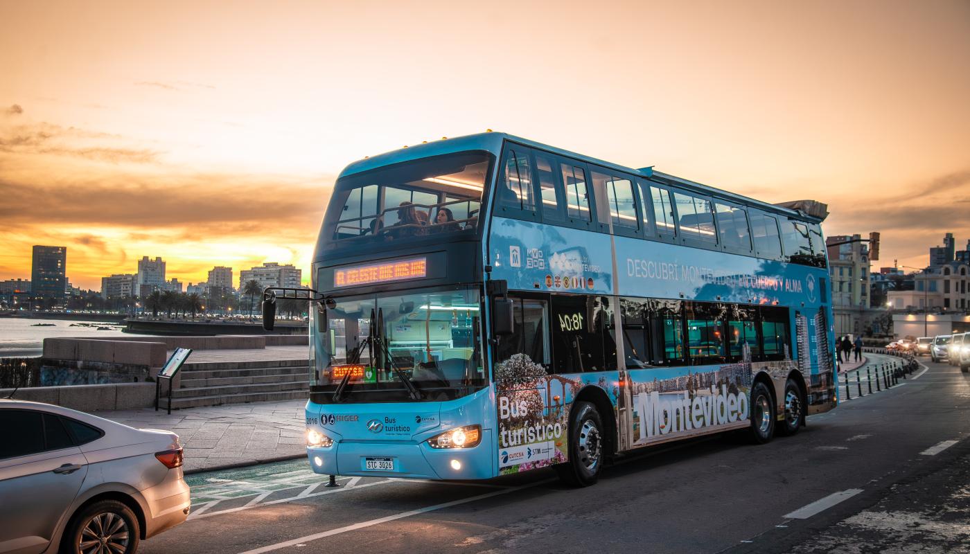 bus turístico de montevideo con la rambla y atardecer de en el fondo