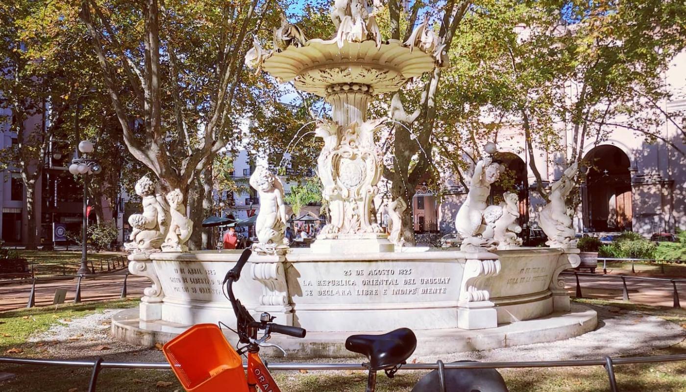 bicileta d ela empresa orange bike, naranja en primer plano de fondo la fuente de la plaza matriz