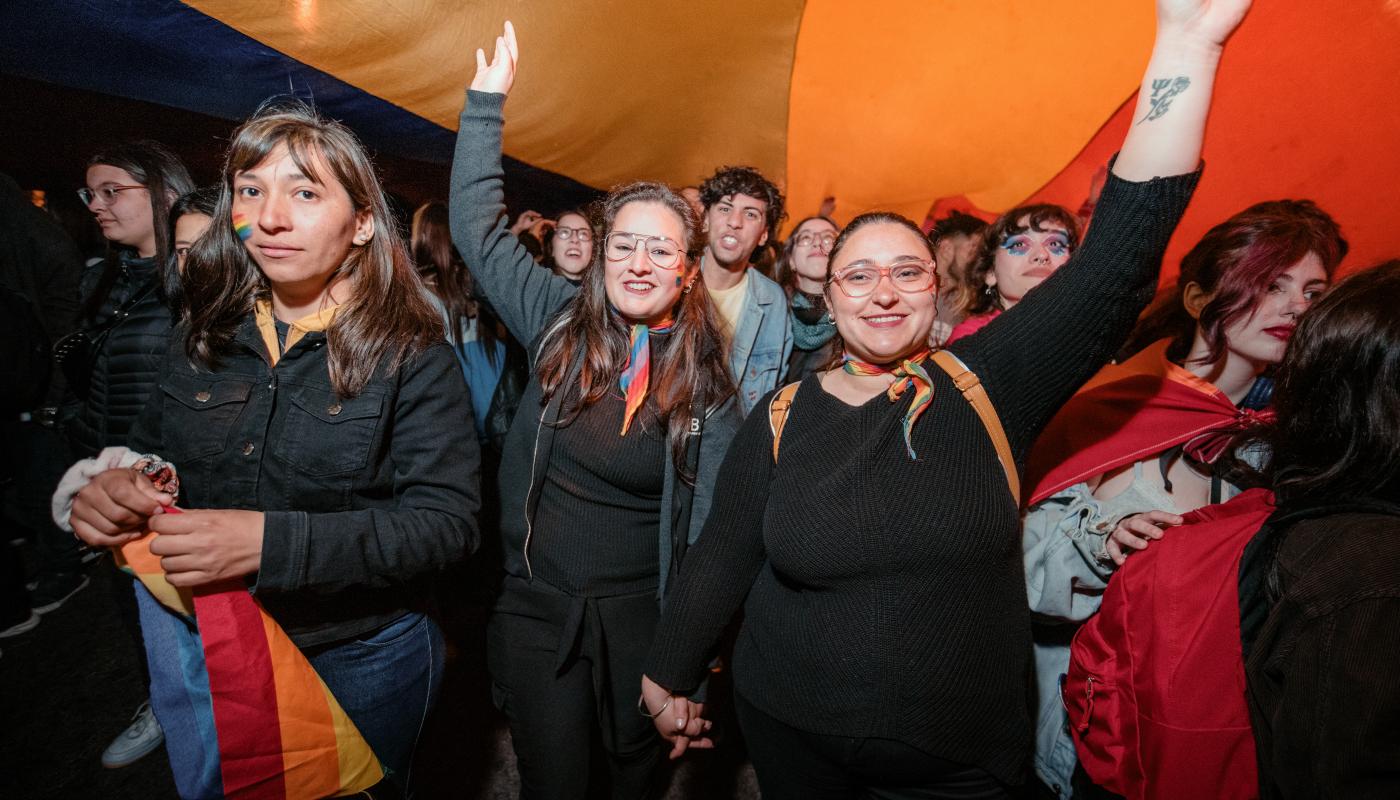 tres mujeres abajo de la bandera lgbtq+ en la marcha de la diversidad