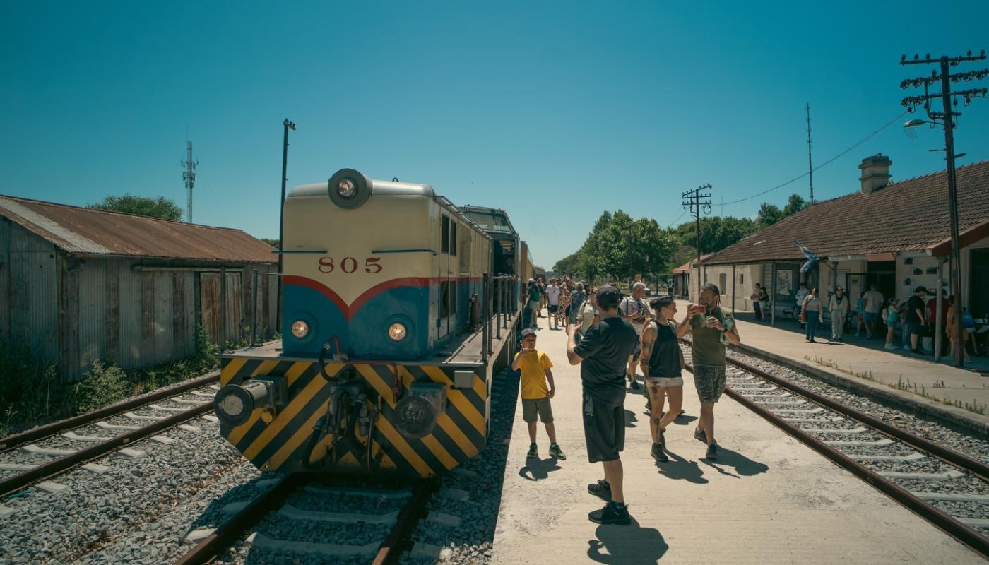Foto de la locomotra principal del tren junto a gente esperando en la estación