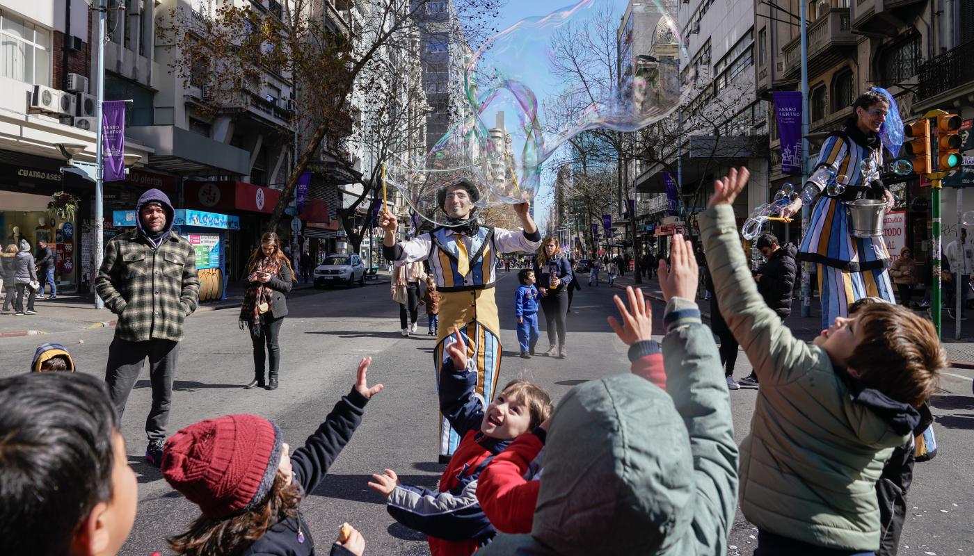grupo de niños en 18 de julio hecha peatonal por el día d elas infancias juagando con burbujas gigantes y payasos