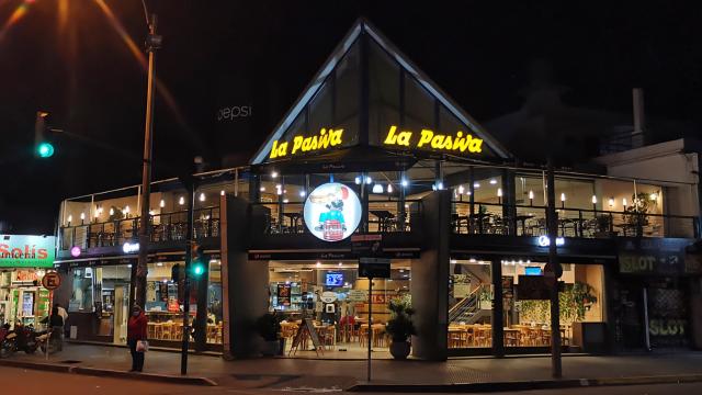 Foto nocturna de la fachada vidriada del local con terraza muy iluminado 