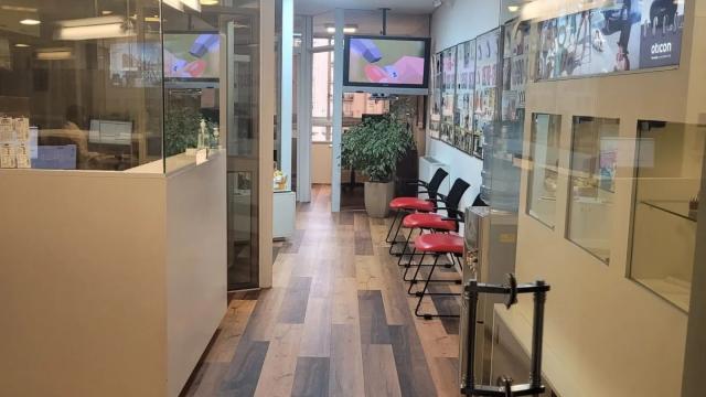 Sala de espera con piso de madera y escritorio de recepción. Mucho vidrio. Cartelería alusiva. 