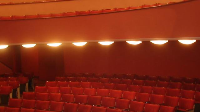 Sala frontal estilo “a la italiana” con forma de herradura. Escenario. Butacas rojas. Al fondo paneles de madera y luces para las obras.