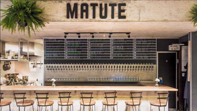 Plano principal de la barra en madera con sus correspondientes sillas y canillas de cerveza tirada.  Decoración rústica con platas y letrero Matute al fondo en metal
