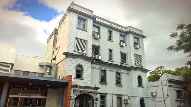 Edificio antiguo de color blanco de dos pisos. Entrada vidriada en forma de arco. 