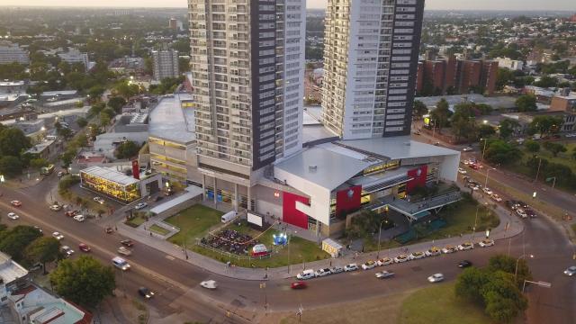 Foto aérea que muestra todo el shopping, su entrada y dos torres de apartamentos grandes detrás. 