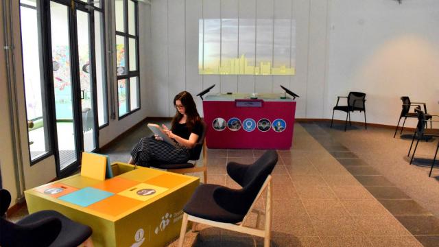 visitante sentado en la oficina de información Turística vidriada utilizando las tablets brindadas por el Servicio. Al fondo se encuentra una mesa interactiva