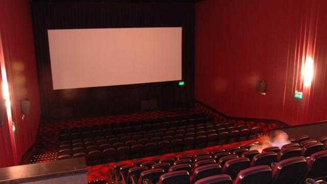 Foto desde atrás con las butacas rojas en dos niveles y pantalla para proyectar al frente.
