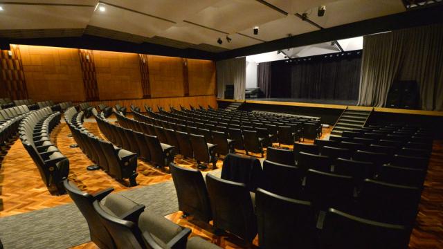 sala del auditorio con butacas color negro sobre piso de madera claro enfrentadas a escenario grande con telones y en altura