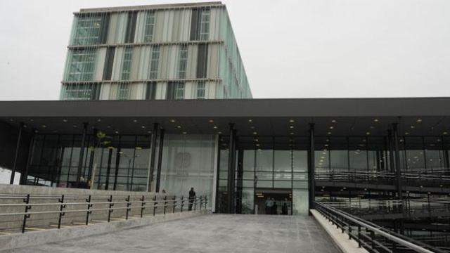 Ingreso mediante rampa de material. Edificio moderno todo vidriado con varios pisos. Formas cuadradas y rectangulares del edificio. 