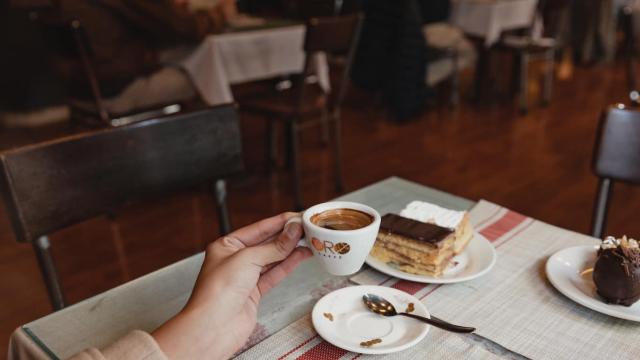 primer plano de mujer merendando una torta de cafe al fondo el local de varias mesas decorado con maderas antiguas