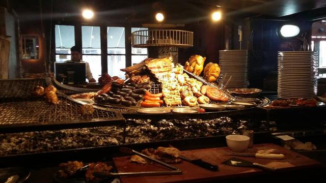 foto de una gran parrillla con muchos tipos de carne y una tabla con utensillo  como ser cuchillo y cortes de carne