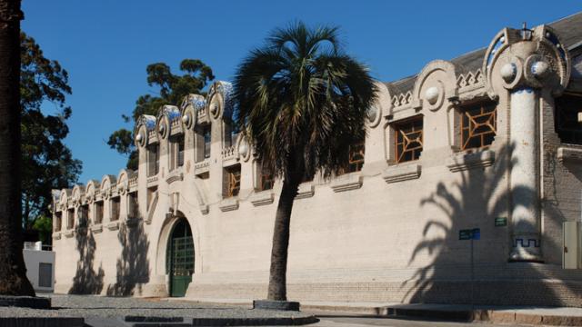 Imagen de uno de los galpones de la Rural del Prado. Un edificio antiguo con una gran puerta verde al medio. La puerta está inserta en un gran marco circular que forma parte del edificio.