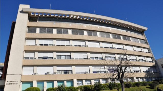 Edificio moderno con varios pisos de colores claros. Jardín al frente. 