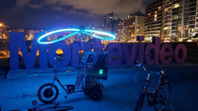 Foto nocturna del Cartel de Montevideo con una bicicleta iluminada con un aro de luz y parlantes