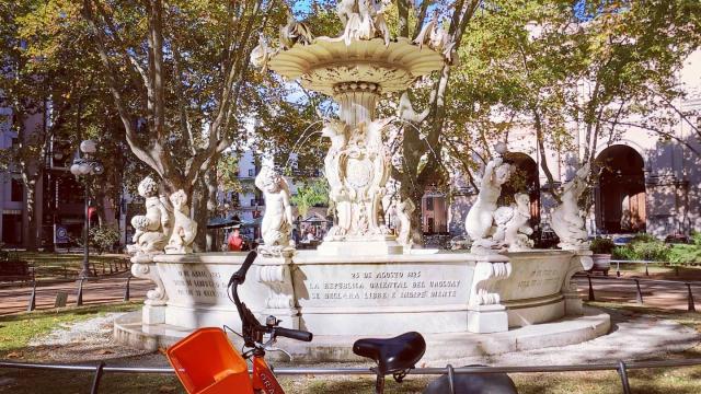 bicileta d ela empresa orange bike, naranja en primer plano de fondo la fuente de la plaza matriz