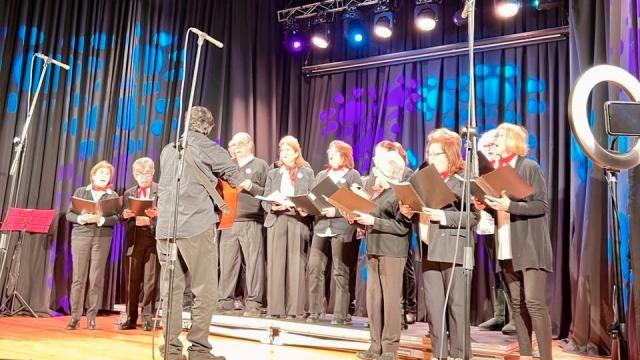coro de personas vestidas de negro sobre escenario iluminado con fonfo de coleres de luces azule sy violetas