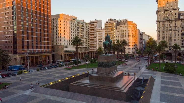 Panóramica de la Plaza Independencia. Monumento de Artigas a caballo en el centro de la plaza. Debajo el mausoleo. Alrededor edificios históricos y palmeras.