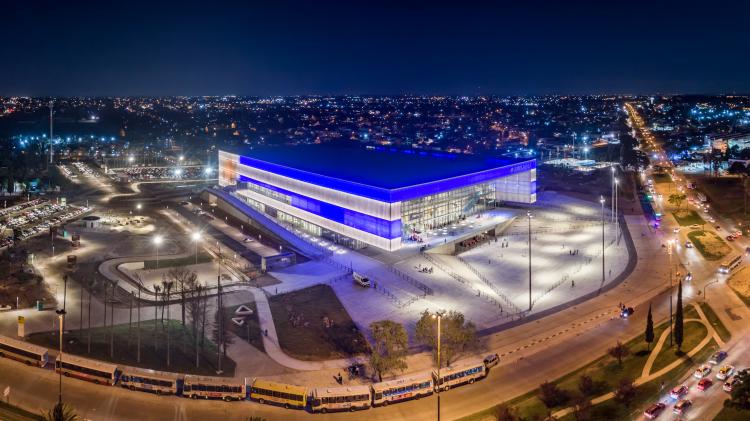 foto aérea de la gran estructura en forma de contenedor del antel arena, muy iluminado tanto la estructura como su plaza multipropósito , también se ven las avenidas que rodean el complejo con buses de transporte