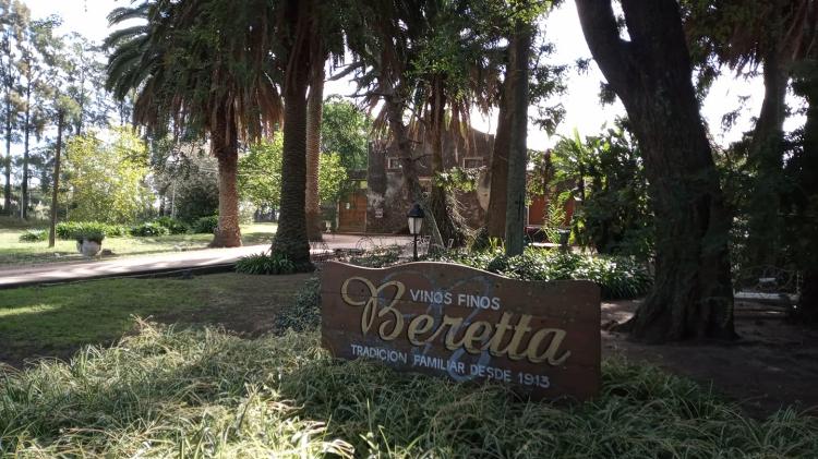 Parque arbolado principal de ingreso indicando Bodega Beretta con letrero de madera. Casa principal al fondo. 