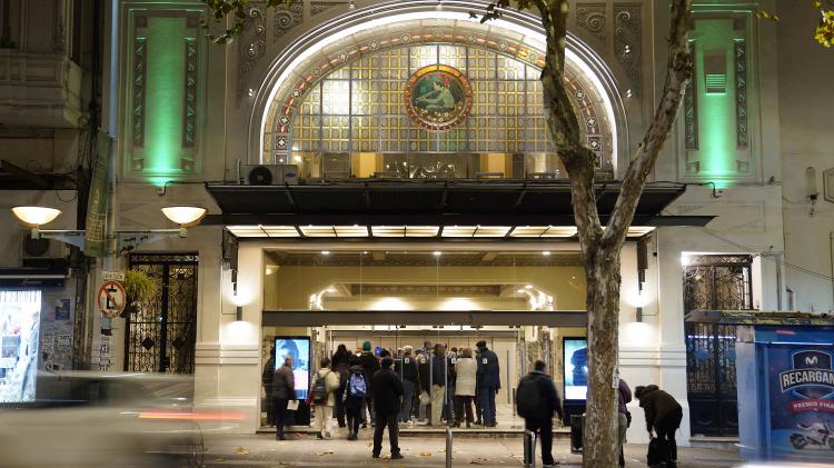Fachada nocturna de la Sala. Se destaca su vitral principal de época iluminado. Detalles art decó en la fachada y puerta de ingreso con gente.