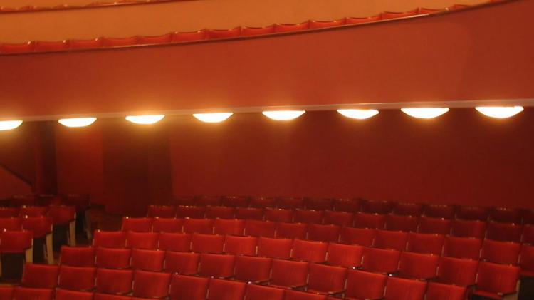 Sala frontal estilo “a la italiana” con forma de herradura. Escenario. Butacas rojas. Al fondo paneles de madera y luces para las obras. 