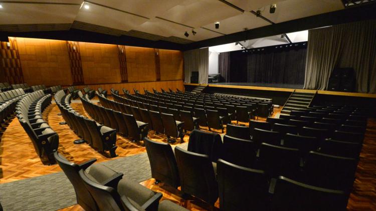 sala del auditorio con butacas color negro sobre piso de madera claro enfrentadas a escenario grande con telones y en altura