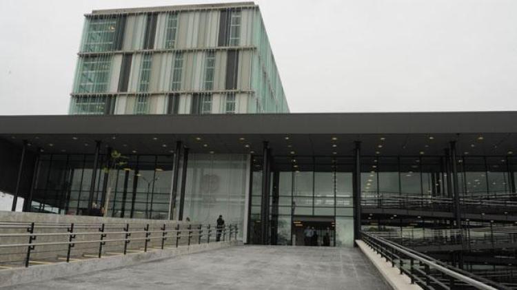 Ingreso mediante rampa de material. Edificio moderno todo vidriado con varios pisos. Formas cuadradas y rectangulares del edificio. 