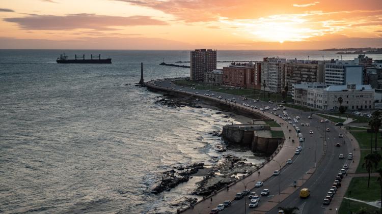 Vista aérea de la Rambla al atardecer. A un costado está el mar y al otro, la ciudad. Al medio, una ancha avenida por donde circulan varios vehículos.
