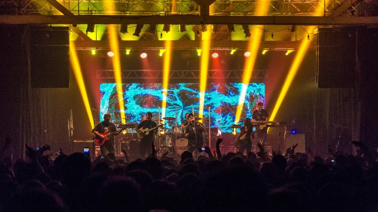 foto nocturna de la sala con mucha gente de pie mirandi hacia el escenario con una bande de rock y gran iluminación de colores